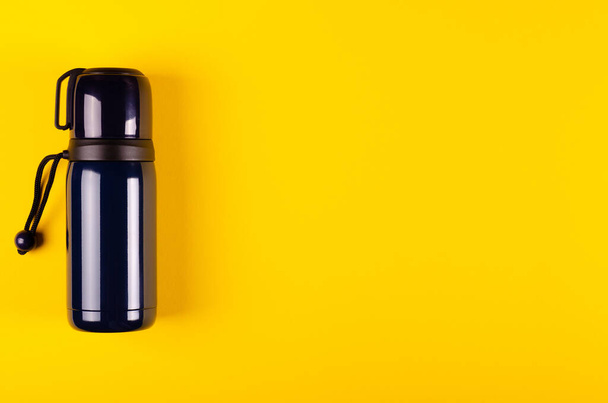 Dark thermos composition on yellow background. Flat lay - Photo, image