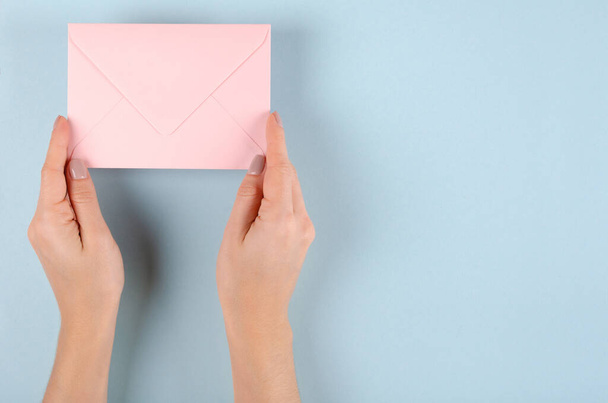 Hand with pink paper envelope composition on blue background. - Fotoğraf, Görsel