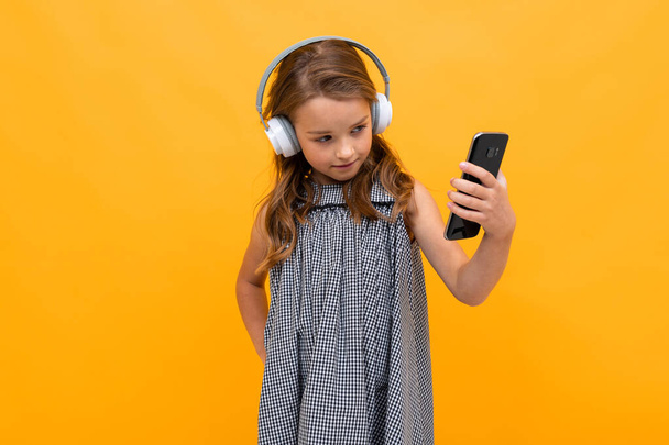 cute little girl listening to music posing against orange background - Фото, зображення