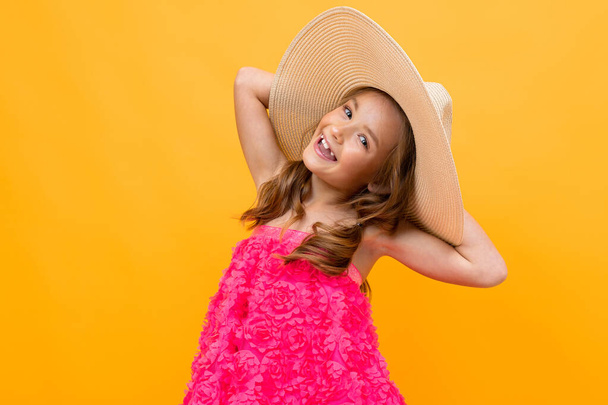 beautiful emotional little girl in straw hat posing against orange background  - Photo, image