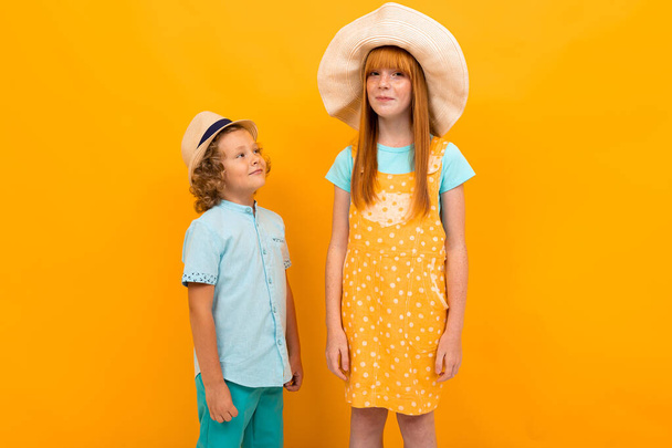 Csinos tizenéves lány vörös haj és kisfiú pózol narancssárga háttér  - Fotó, kép
