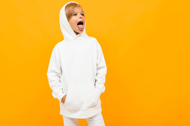 emotionele jongen in wit hoodie poseren tegen oranje achtergrond - Foto, afbeelding
