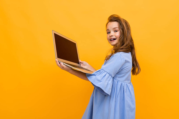 cute little girl z laptopem na pomarańczowym tle  - Zdjęcie, obraz