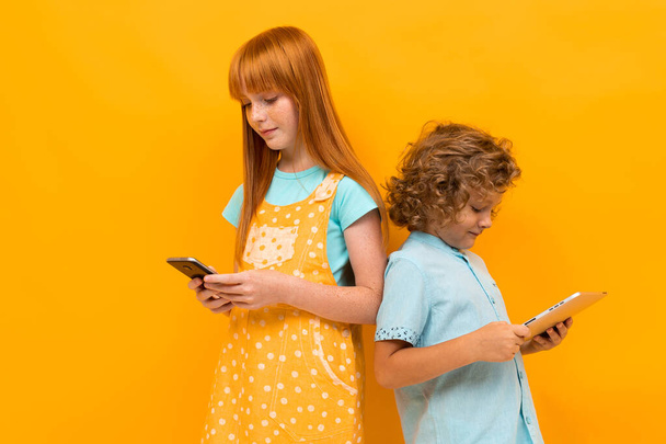 hübsches Teenager-Mädchen mit roten Haaren und kleinem Jungen posiert vor orangefarbenem Hintergrund  - Foto, Bild
