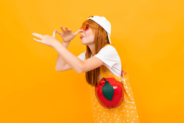 emotional ginger girl in sunglasses posing against orange background  - Photo, image