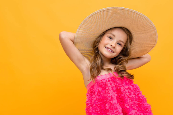 beautiful emotional little girl in straw hat posing against orange background  - Foto, Imagen