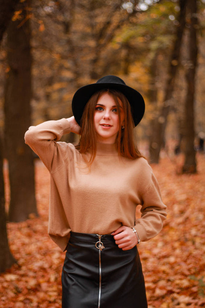 Autumn girl in the park. Sweater, hat and leather skirt. Stylish - 写真・画像