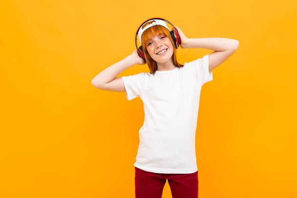 χαριτωμένο κορίτσι τζίντζερ θέτει σε πορτοκαλί φόντο με ακουστικά - Φωτογραφία, εικόνα