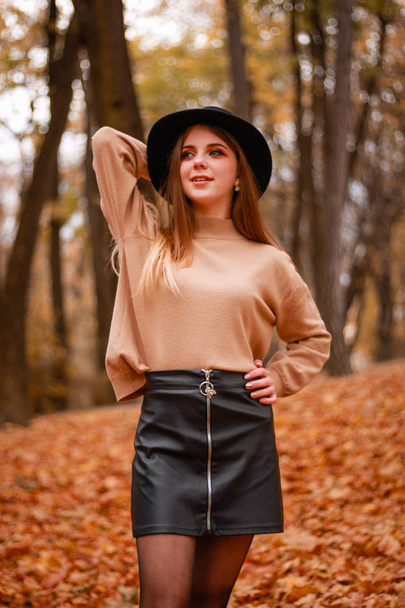 Autumn girl in the park. Sweater, hat and leather skirt. Stylish - Photo, Image