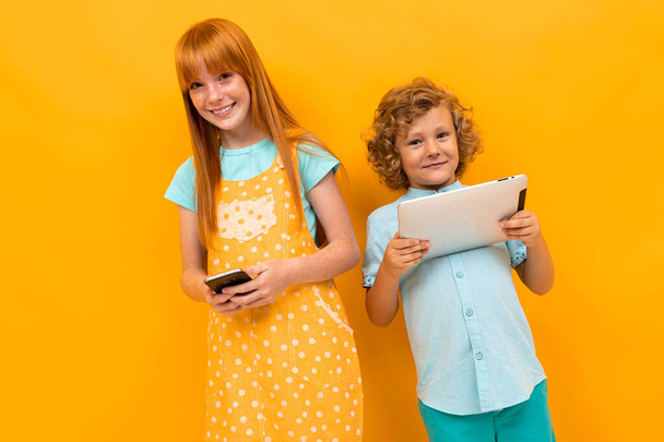 Красивая девочка-подросток с рыжими волосами и маленьким мальчиком позирует на оранжевом фоне
  - Фото, изображение