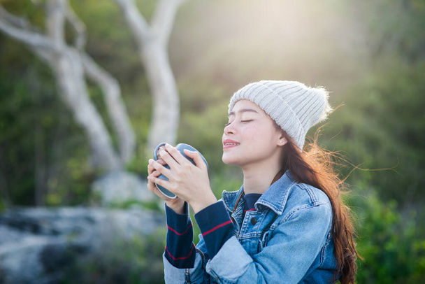 Счастливая азиатская женщина с кружкой кофе на фоне природы, камера
 - Фото, изображение