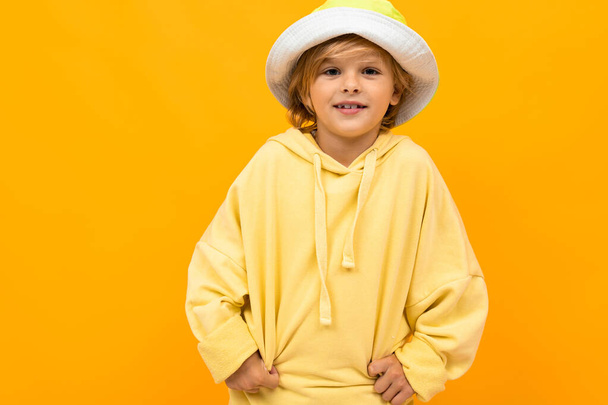 módní chlapec v mikině a čepici pózující proti oranžové  - Fotografie, Obrázek