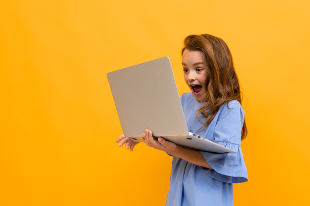 χαριτωμένο κοριτσάκι με φορητό υπολογιστή σε πορτοκαλί φόντο  - Φωτογραφία, εικόνα