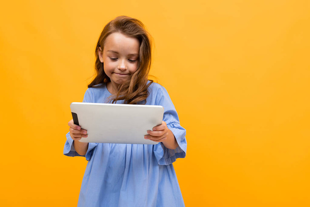 cute little girl with tablet posing against orange background  - Photo, Image
