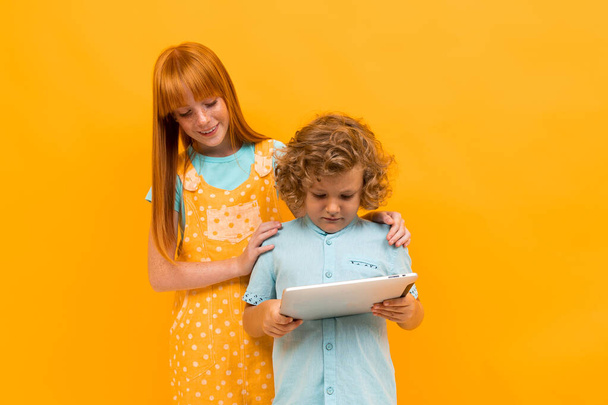 Pretty teenage girl with red hair and little boy posing against orange background  - Foto, afbeelding