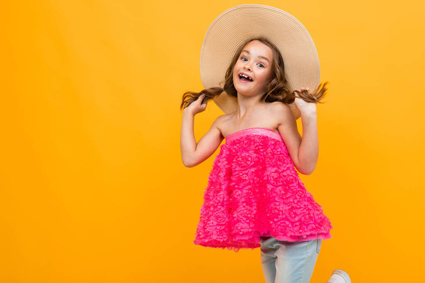 красивая эмоциональная маленькая девочка в соломенной шляпе позирует на оранжевом фоне
  - Фото, изображение