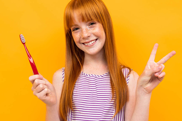 Pretty teenage girl with red hair posing with Toothbrush against orange background  - Foto, immagini