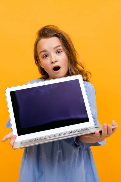 χαριτωμένο κοριτσάκι με φορητό υπολογιστή σε πορτοκαλί φόντο  - Φωτογραφία, εικόνα