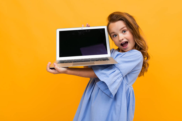 Nettes kleines Mädchen mit Laptop vor orangefarbenem Hintergrund  - Foto, Bild