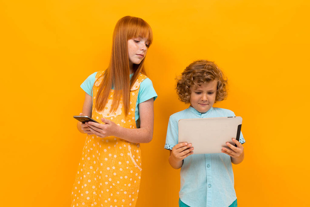Pretty teenage girl with red hair and little boy posing against orange background  - Foto, Bild