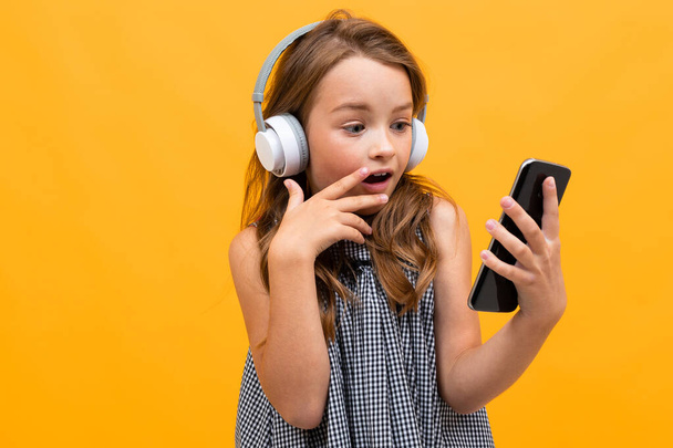 cute little girl listening to music posing against orange background - Foto, Imagem