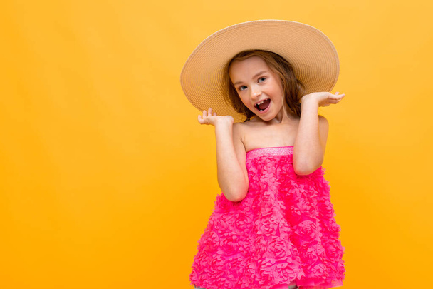 beautiful emotional little girl in straw hat posing against orange background  - 写真・画像