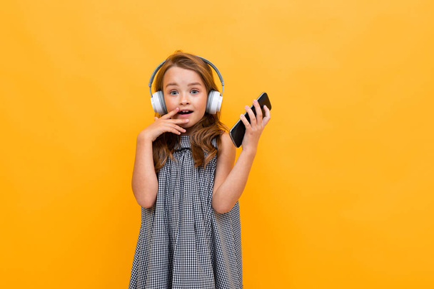 cute little girl listening to music posing against orange background - Foto, imagen