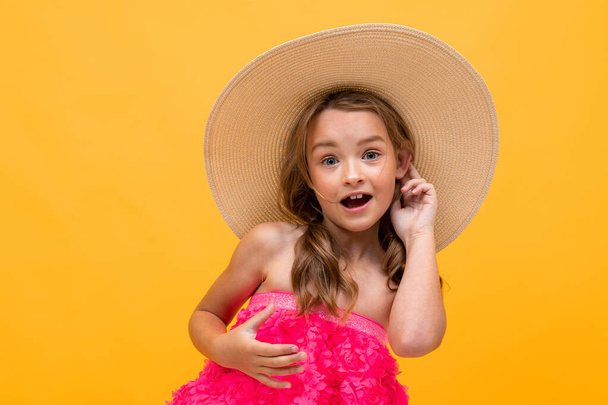 piękne emocjonalne dziewczynka w słomkowym kapeluszu pozowanie na pomarańczowym tle  - Zdjęcie, obraz