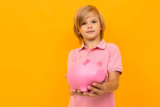 little boy with piggy bank against orange - Photo, Image