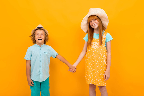 Pretty teenage girl with red hair and little boy posing against orange background  - Zdjęcie, obraz