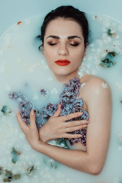 güzel bir genç kız portresi rahatlatıcı ve süt ve leylak çiçekleri ile banyoda istirahat - Fotoğraf, Görsel