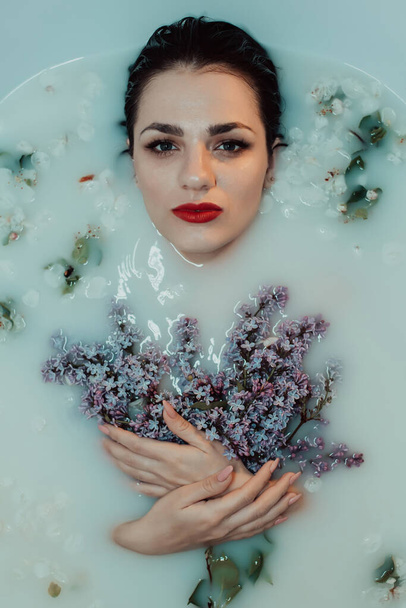 portrait of a beautiful girl with red lipstick and makeup relaxing and resting in the bath with milk and lilac - Photo, image