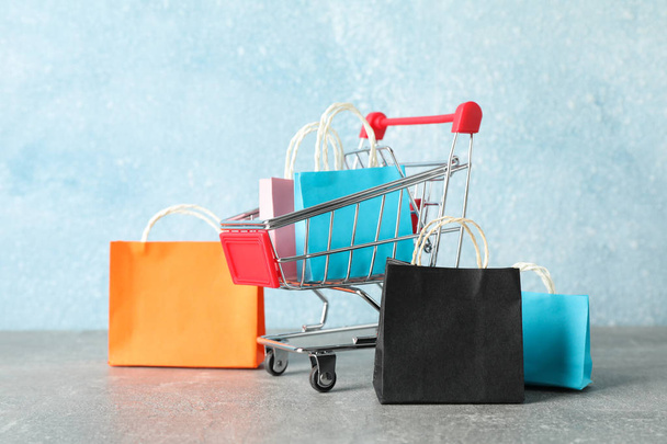 Small shopping cart and paper bags on grey background, copy spac - Photo, Image