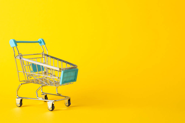 Small shopping cart on yellow background, space for text - Photo, image
