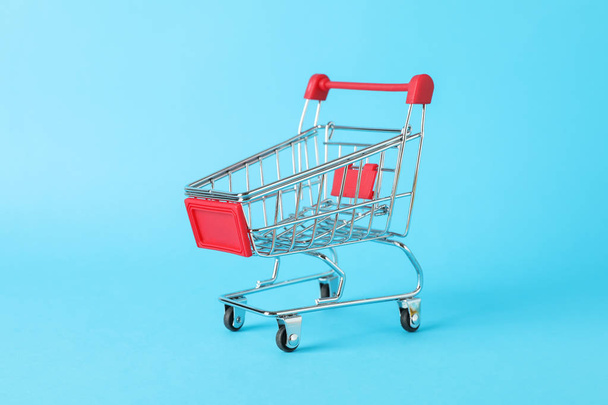 Small shopping cart on blue background, space for text - Foto, Bild