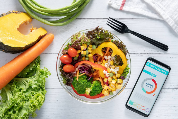 Calories counting , diet , food control and weight loss concept. Calorie counter application on smartphone screen at dining table with salad, fruit juice, bread and vegetable - Fotoğraf, Görsel