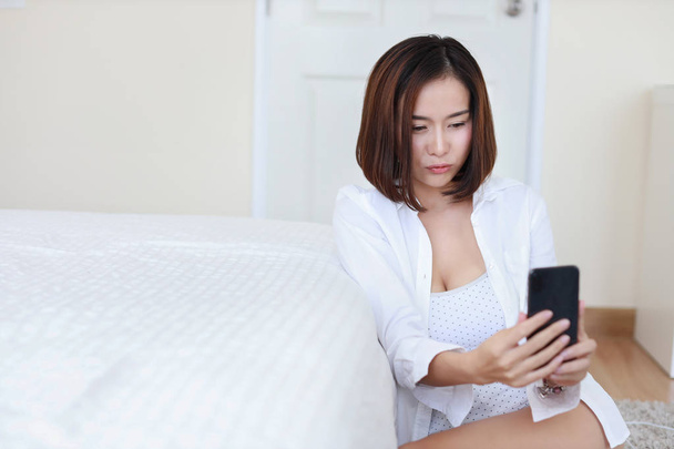 jeune attrayant asiatique femme portant chemise blanche en utilisant VDO appel à partir de téléphone cellulaire et donner baiser dans la chambre blanche
  - Photo, image