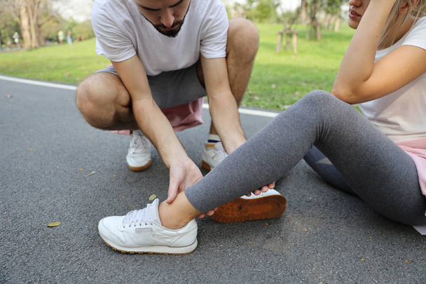 man helping jogger woman who hurt the ankle from too much exercise in the park - Foto, afbeelding