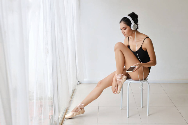 bela saudável e desportivo asiático jovem mulher no preto sportswear com fone de ouvido, usando celular enquanto pratica balé
 - Foto, Imagem