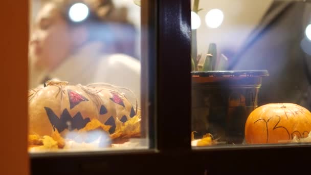Abóboras de laranja com símbolos de Véspera de Todos os Santos em uma janela de café de rua. Atrás do vidro
 - Filmagem, Vídeo