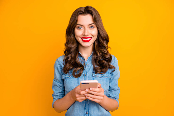 Photo of trendy cheerful cute nice sweet pretty girl smiling toothily holding phone with hands expressing positive reaction to received messages isolated over yellow vivid color background - Zdjęcie, obraz