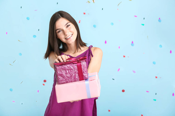 schöne junge Frau mit Geschenken und fallendem Konfetti auf farbigem Hintergrund - Foto, Bild