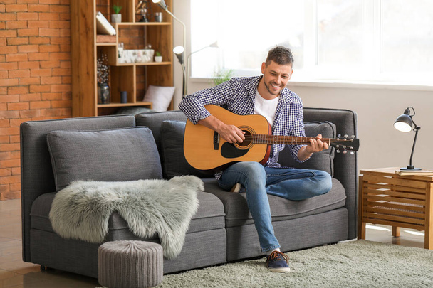 Όμορφος άντρας παίζει κιθάρα στο σπίτι. - Φωτογραφία, εικόνα