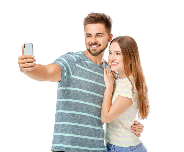 Portrait of happy young couple taking selfie on white background - Foto, Imagen