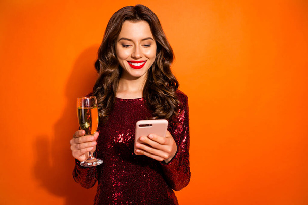 Close-up portrait of her she nice attractive pretty chic gorgeous cheerful cheery wavy-haired girl drinking champagne typing sms message isolated over bright vivid shine vibrant orange color - Foto, imagen
