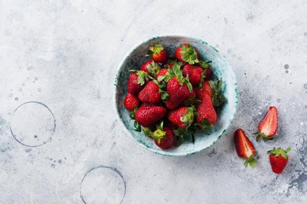 Fresh strawberry in old ceramic bowl rustic with green leaves on gray concrete background. Healthy breakfast concept. Top view. - Foto, afbeelding