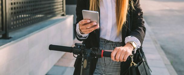 E-scooterlı tanınmayan iş kadını cep telefonuna bakıyor. - Fotoğraf, Görsel