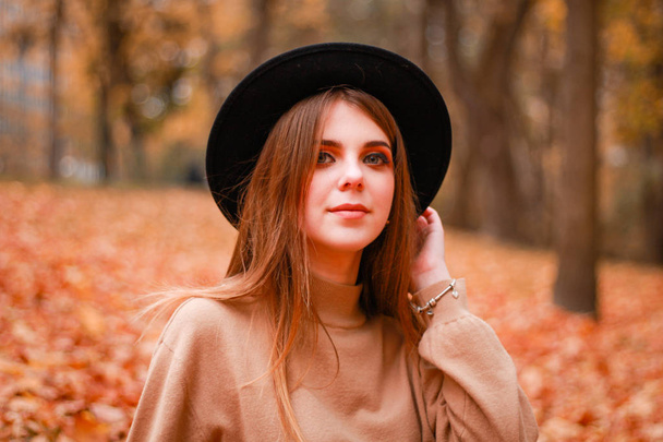 Το κορίτσι του φθινοπώρου στο πάρκο. Πουλόβερ, καπέλο και δερμάτινη φούστα. Κομψό - Φωτογραφία, εικόνα