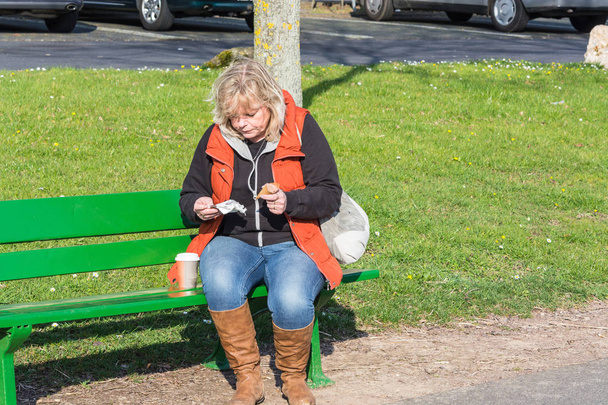 Femme assise sur un banc et mangeant une glace
              - Photo, image