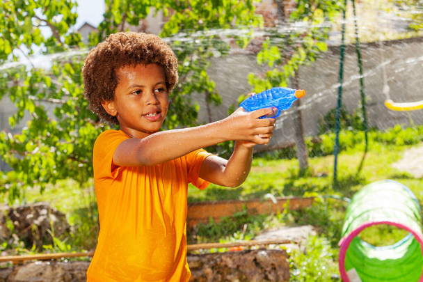 Guapo chico negro disparando con pistola de agua jugando juego activo en el jardín
 - Foto, Imagen